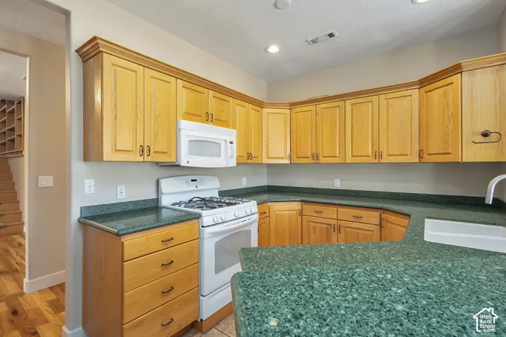 L-shaped kitchen featuring light wood cabinetry, green speckled countertops, a built-in microwave, and a gas range
