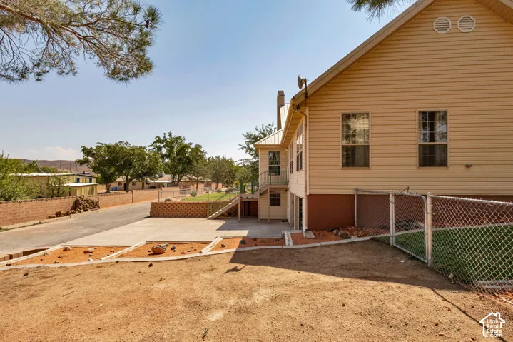 Siding exterior with multiple windows, chain link fencing, a paved driveway, and mature landscaping