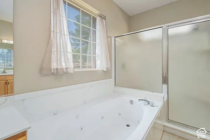 Primary suite with Integrated jetted tub with white surround, separate shower with frosted glass enclosure, and a large window with grid pattern