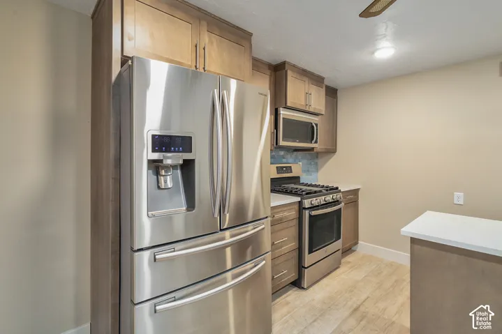 Stainless steel appliances, wood-finish flooring, wood cabinetry, tile backsplash, and light-toned countertops
