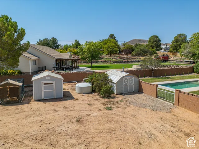 Expansive backyard featuring a rectangular swimming pool, two storage sheds, a separate enclosure, and a large patio area with a pergola