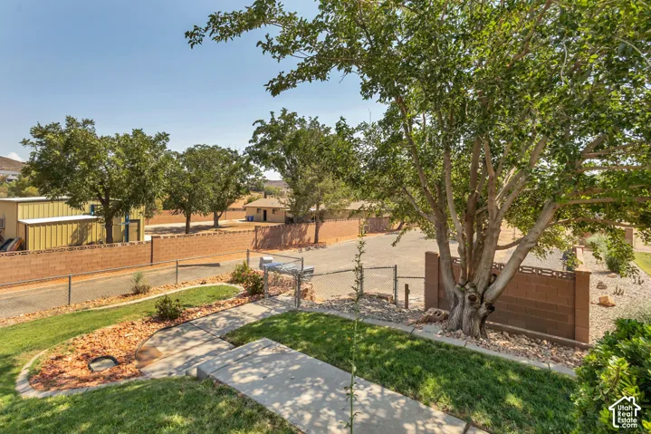 Manicured lawn with concrete pathways and mature trees, featuring a block wall perimeter