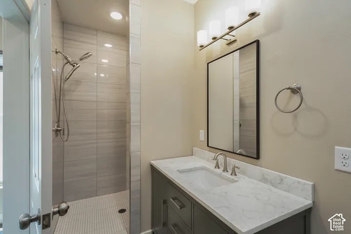 Walk-in shower with large format tile, brushed nickel shower fixtures, vanity with stone-finish countertop, undermount sink, and wall-mounted light fixture