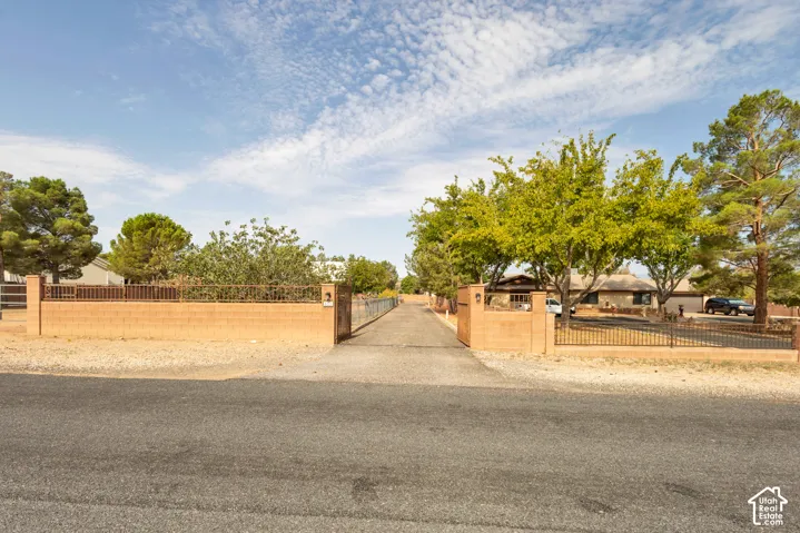 Gated entrance with brick pillars, metal fencing, and mature trees lining a paved driveway