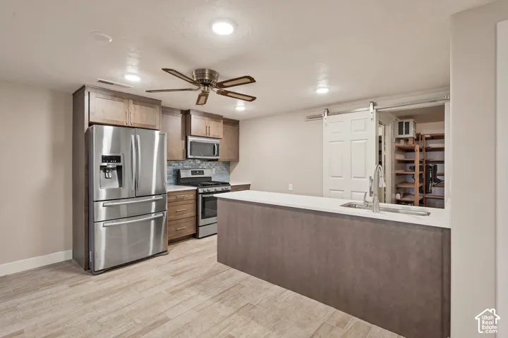 Kitchen featuring stainless steel appliances, wood-finish cabinetry, a large kitchen island with an undermount sink, and wood-finish flooring