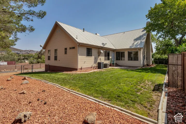 Metal roof, tan siding, multiple windows, grassy lawn, and a stone chip landscaping bed.