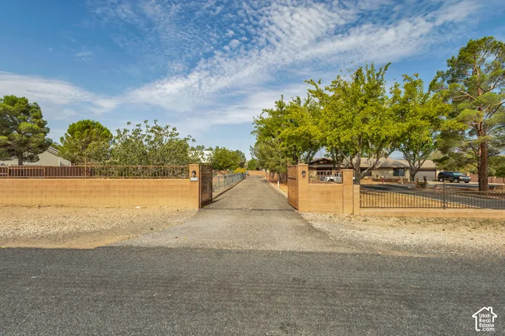 Gated entry with brick pilasters, wrought iron fencing, and an asphalt driveway surrounded by mature trees