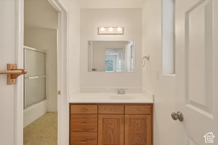 Wood-finish vanity with a white countertop and integrated sink, chrome-finish faucet, and a wall-mounted rectangular mirror