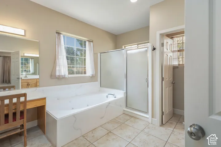 primary suite with Built-in soaking tub, glass-enclosed shower, tiled flooring, vanity with a dedicated seating area, and a large window