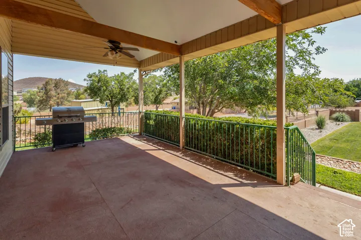 Expansive covered patio with a ceiling fan, exposed wood beams, and a concrete surface
