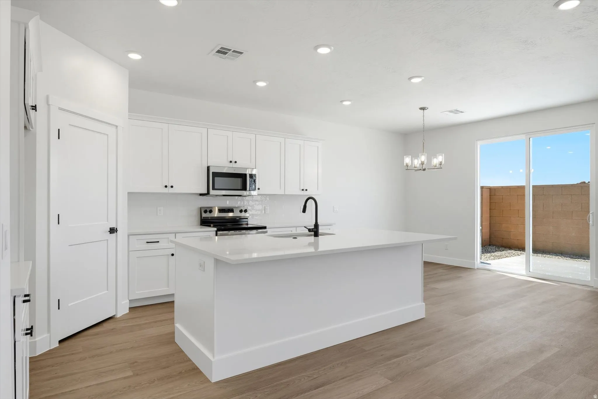 Kitchen featuring white cabinetry, stainless steel appliances, a center island with a sink, and wood-finish flooring