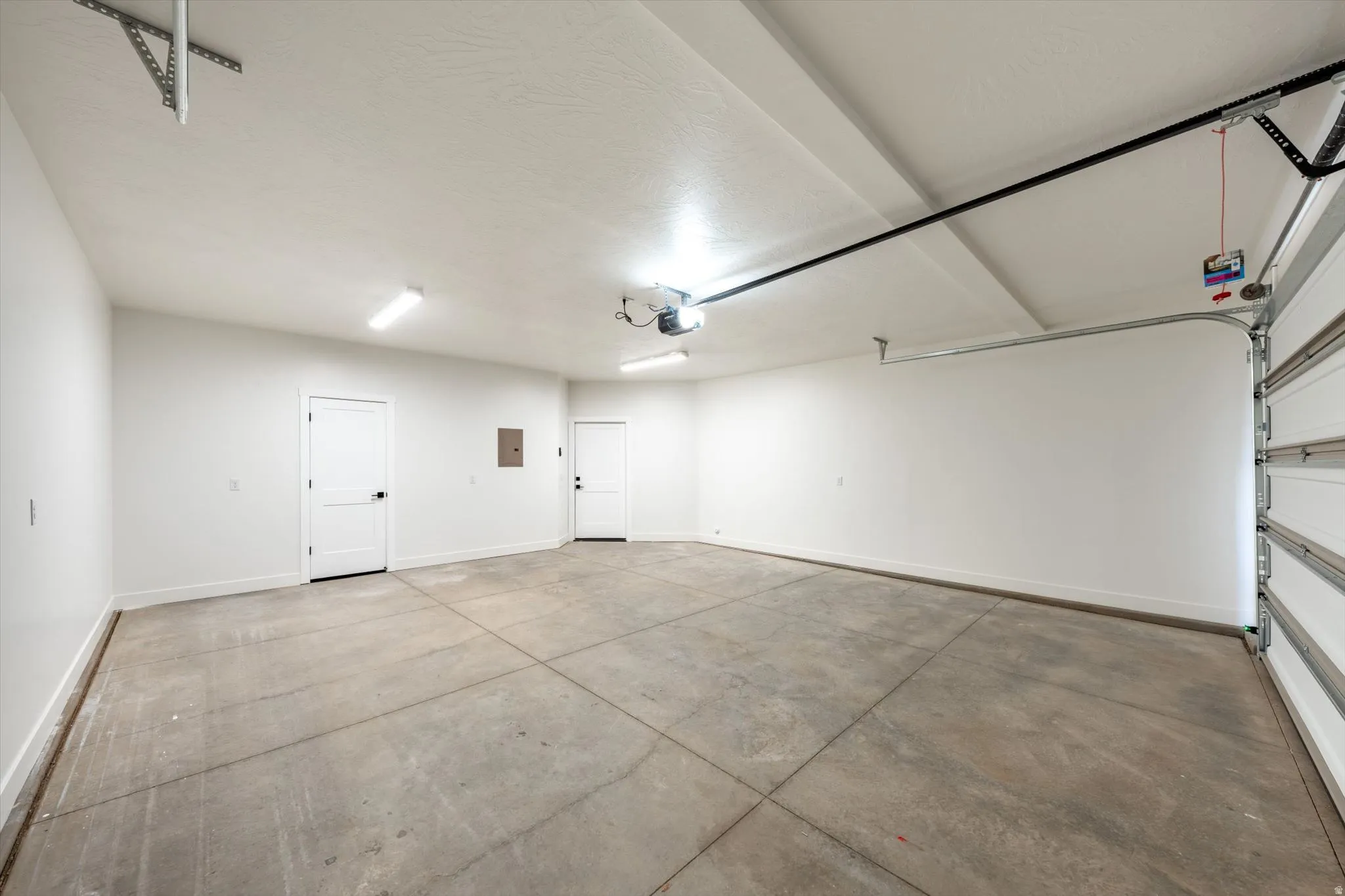 Spacious garage featuring a concrete floor, bright overhead lighting, and two interior access doors