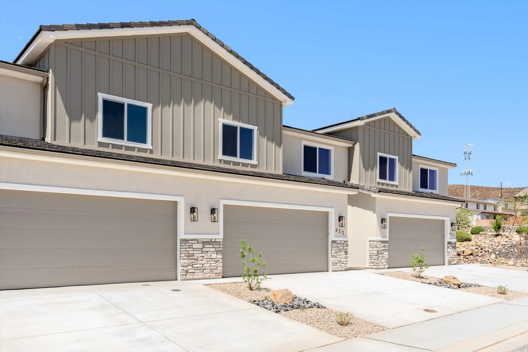 Multi-story residence featuring board and batten siding, stucco exterior, stone veneer accents, individual garage doors, and exterior lighting fixtures