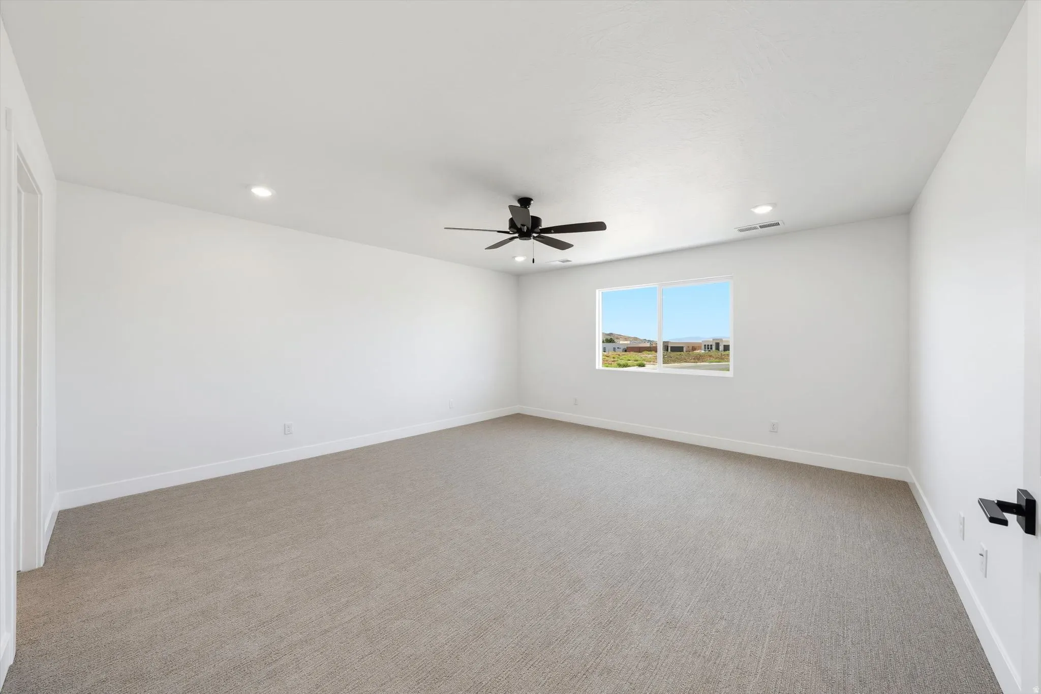 Spacious room featuring neutral carpeting, white walls, recessed lighting, and a ceiling fan