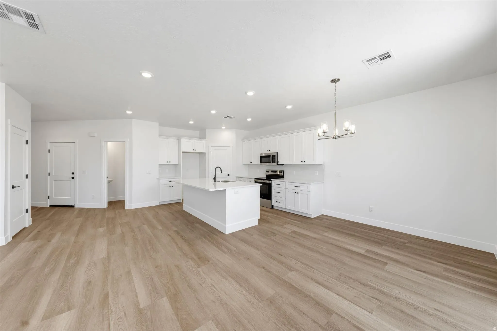 Open-concept living space with wood-finish flooring, recessed lighting, and a modern chandelier