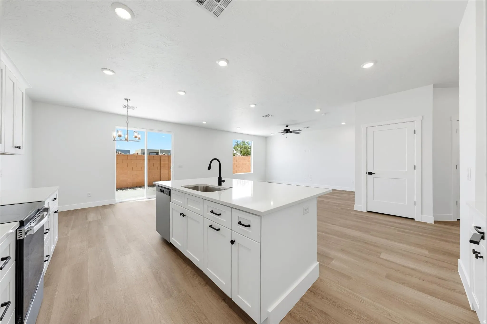 Kitchen featuring white shaker cabinetry, stainless steel dishwasher, an island with an undermount sink and matte black faucet, and wood-finish flooring