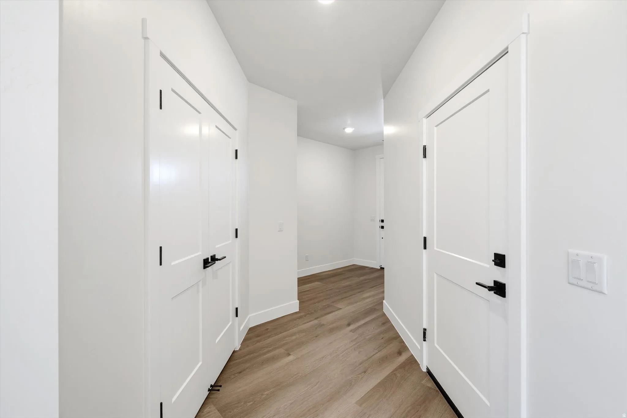 Light wood-finish flooring with white walls and trim, featuring white panel doors with matte black hardware