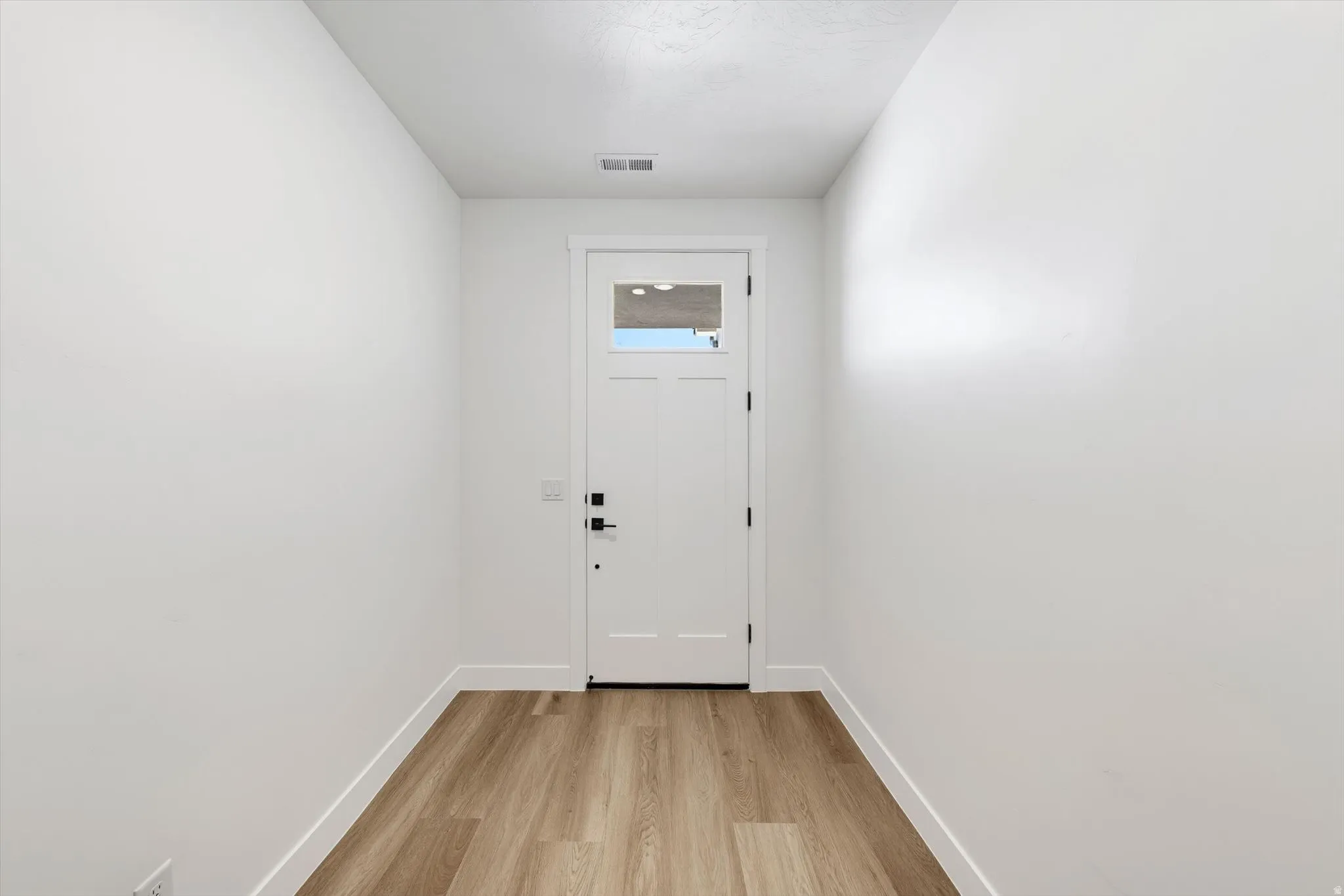 Bright, clean entryway featuring wood-finish flooring, white painted walls, and a white six-panel entry door with dual locks and a small window insert