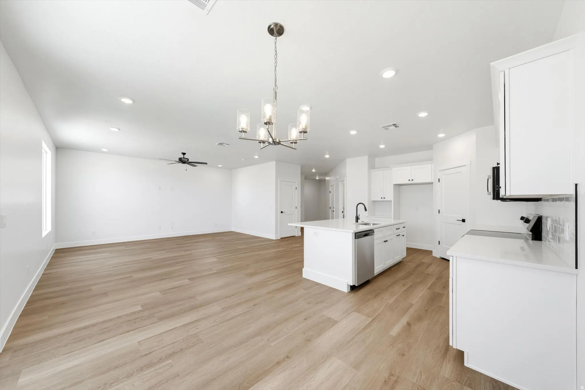 Open-concept living space featuring wood-finish flooring, recessed lighting, a ceiling fan, and an island kitchen with white cabinetry and a built-in dishwasher