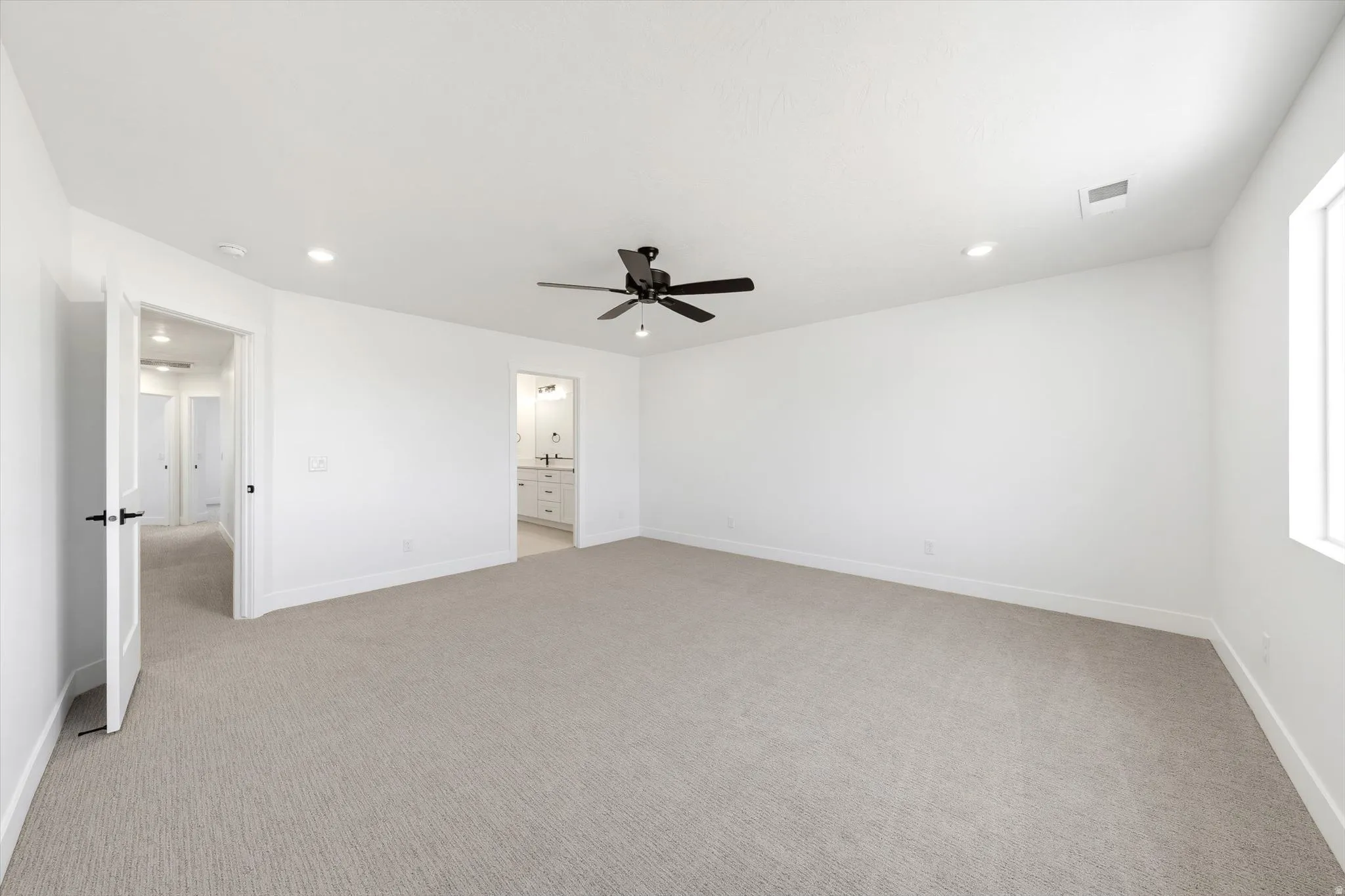 Spacious room featuring neutral carpeting, a ceiling fan, recessed lighting, and a window for natural light