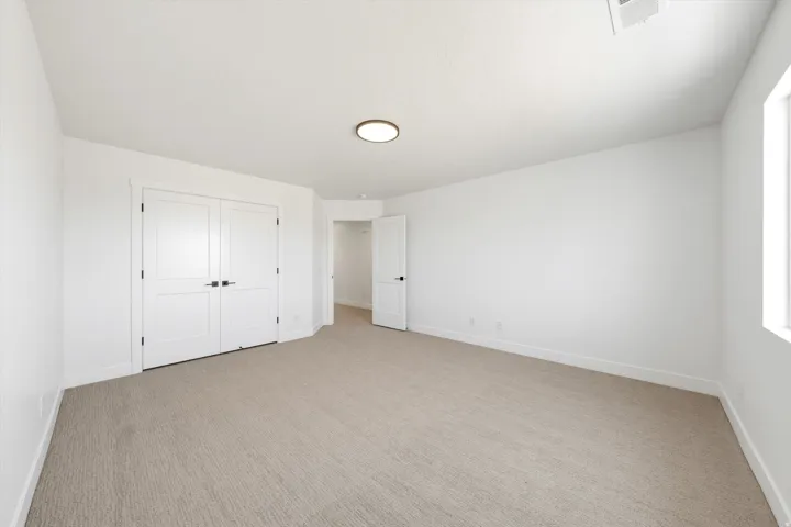Neutral tone carpeting, white walls, flush mount ceiling light, and a prominent window