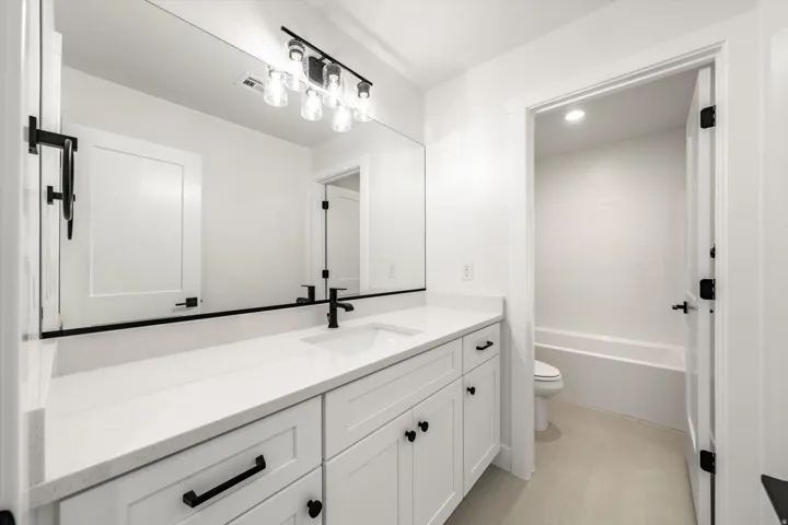 Double vanity with integrated sinks, white cabinetry, matte black hardware, and a large wall-mounted mirror