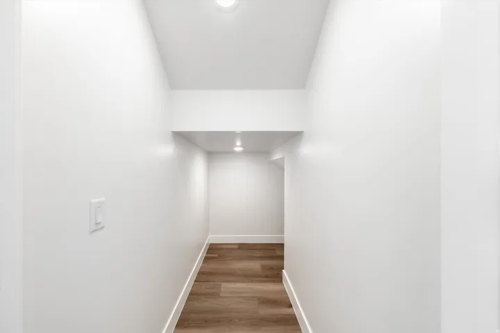 Recessed lighting illuminating wood-finish flooring with white baseboards and walls