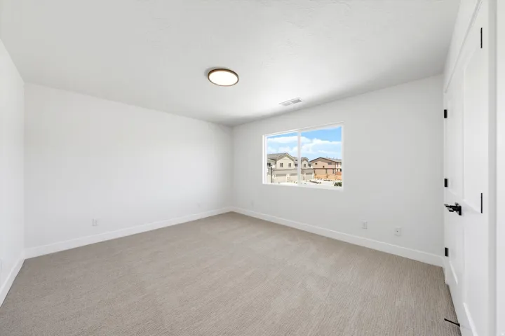 Neutral tone carpet flooring, white painted walls, white trim, white two-panel door with black hardware, and a single window