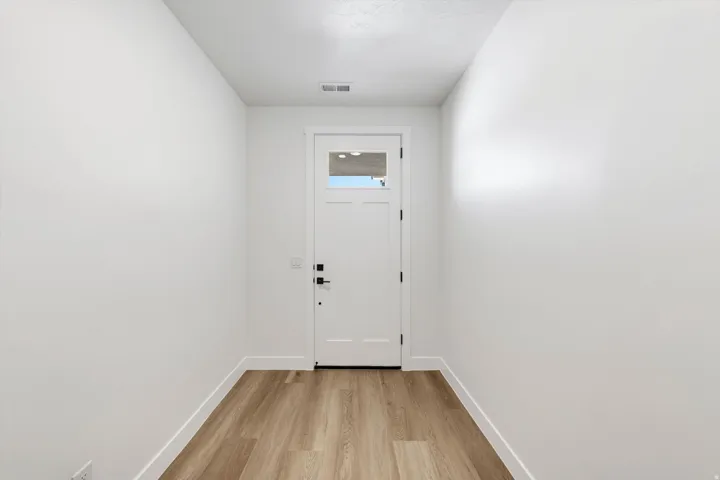 Bright, clean entryway featuring wood-finish flooring, white painted walls, and a white six-panel entry door with dual locks and a small window insert