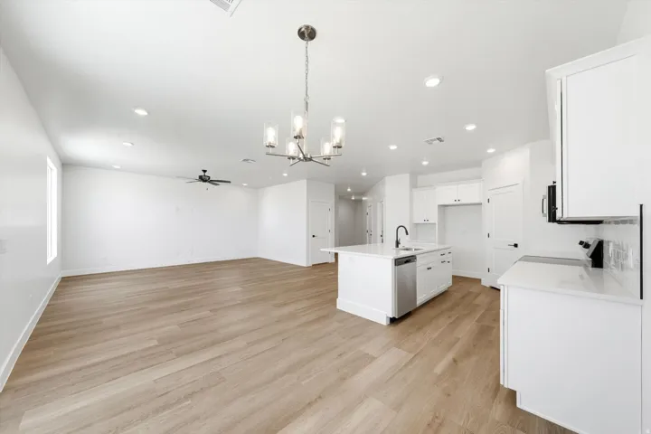 Open-concept living space featuring wood-finish flooring, recessed lighting, a ceiling fan, and an island kitchen with white cabinetry and a built-in dishwasher