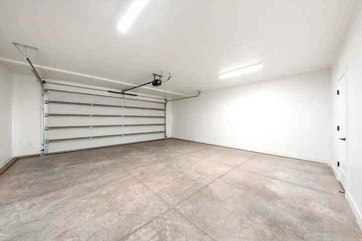 Spacious garage with a sectional overhead door, automatic opener, concrete flooring, and overhead strip lighting