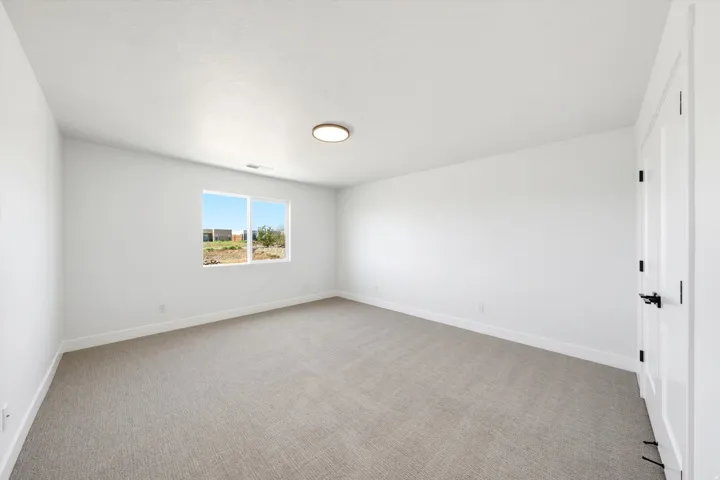 Spacious room featuring neutral carpeting, a large window, white walls, and a modern ceiling light fixture