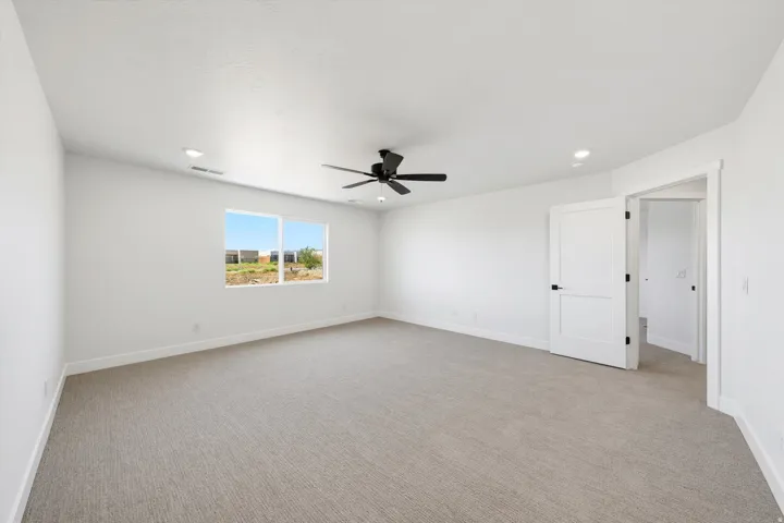 Expansive room featuring light-colored carpeting, white painted walls, and a contemporary black ceiling fan