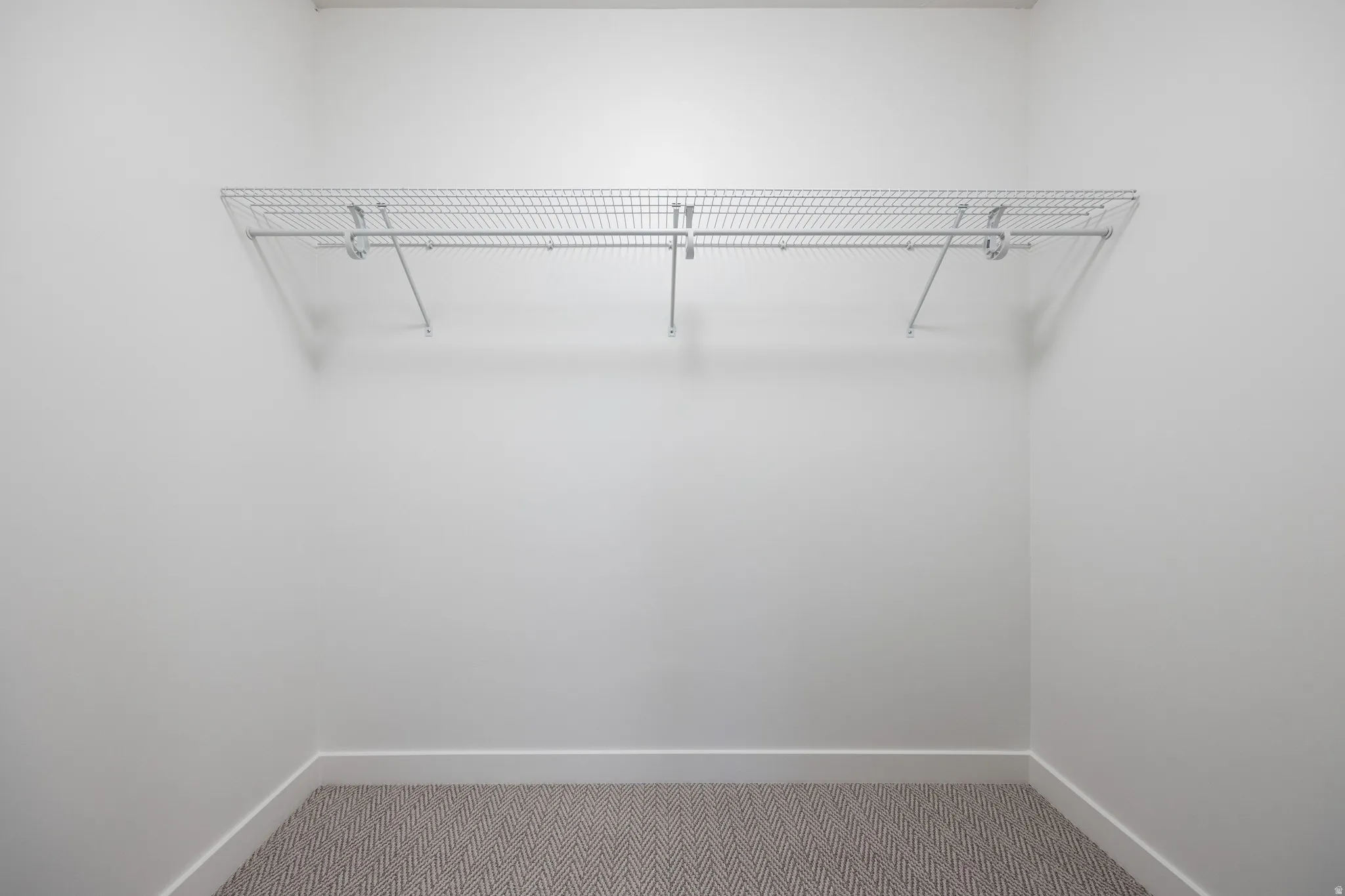 Built-in wire shelving with hanging rod, white walls, and carpet flooring