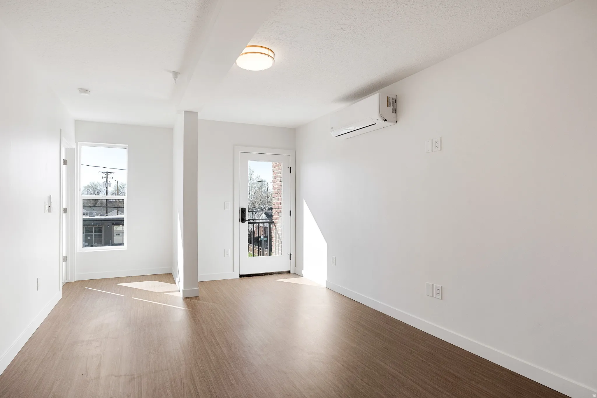 Wood-finish flooring, white walls, flush mount ceiling fixture, split system air conditioning unit, and a glass-paneled door