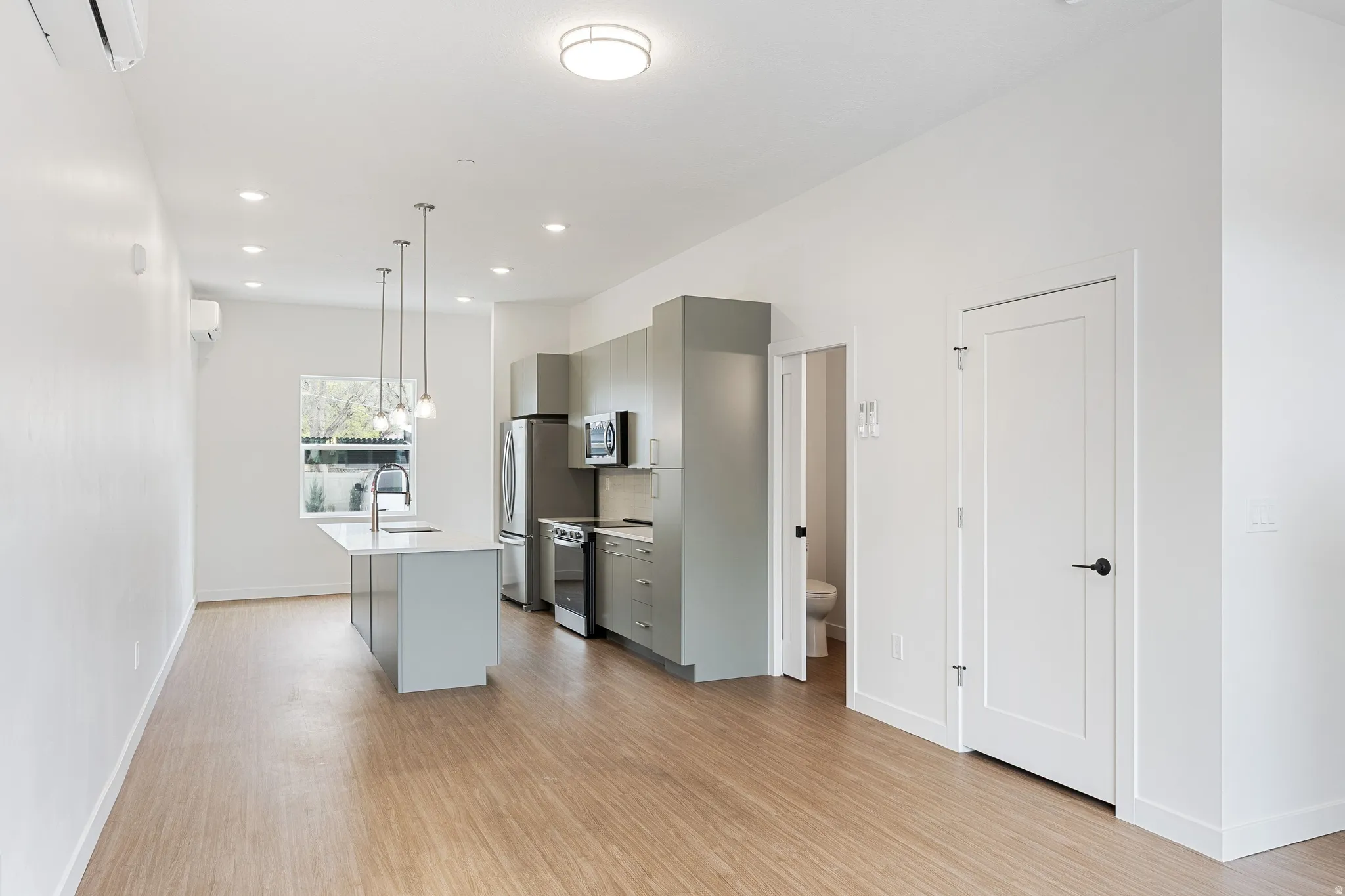 Open-concept living area featuring wood-finish flooring, recessed lighting, and a modern kitchen with a center island and stainless steel appliances