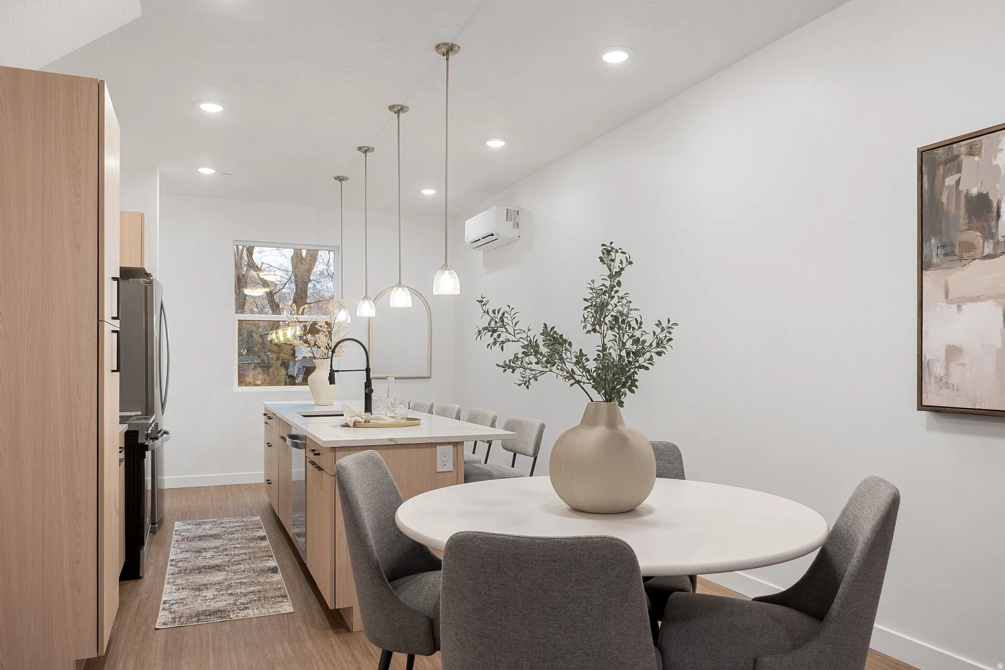 Kitchen featuring wood-finish flooring, recessed lighting, an island with pendant lights, a black gooseneck faucet, and light wood cabinetry