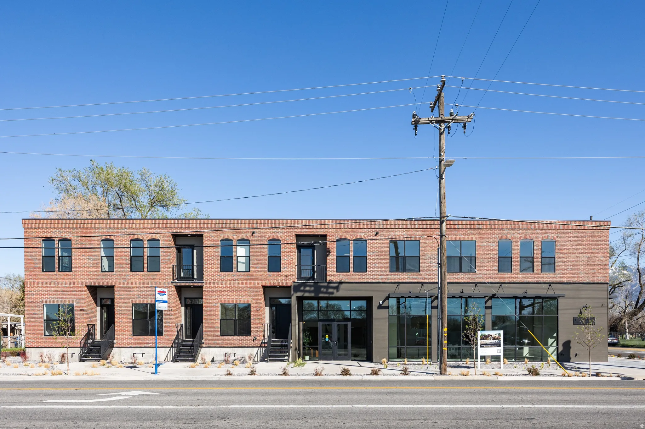 Brick facade with dark-framed windows, ground-level retail spaces, second-story balconies, and multiple entryways