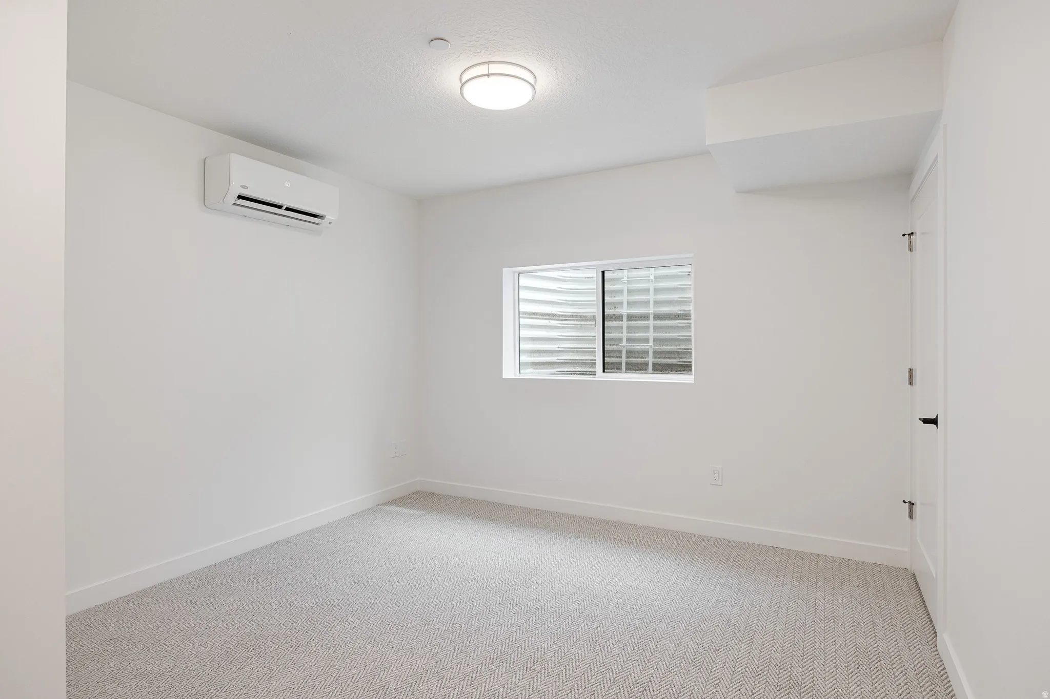 Recessed lighting, wall-mounted air conditioning unit, white trim, textured carpet, and a window with a glass block exterior