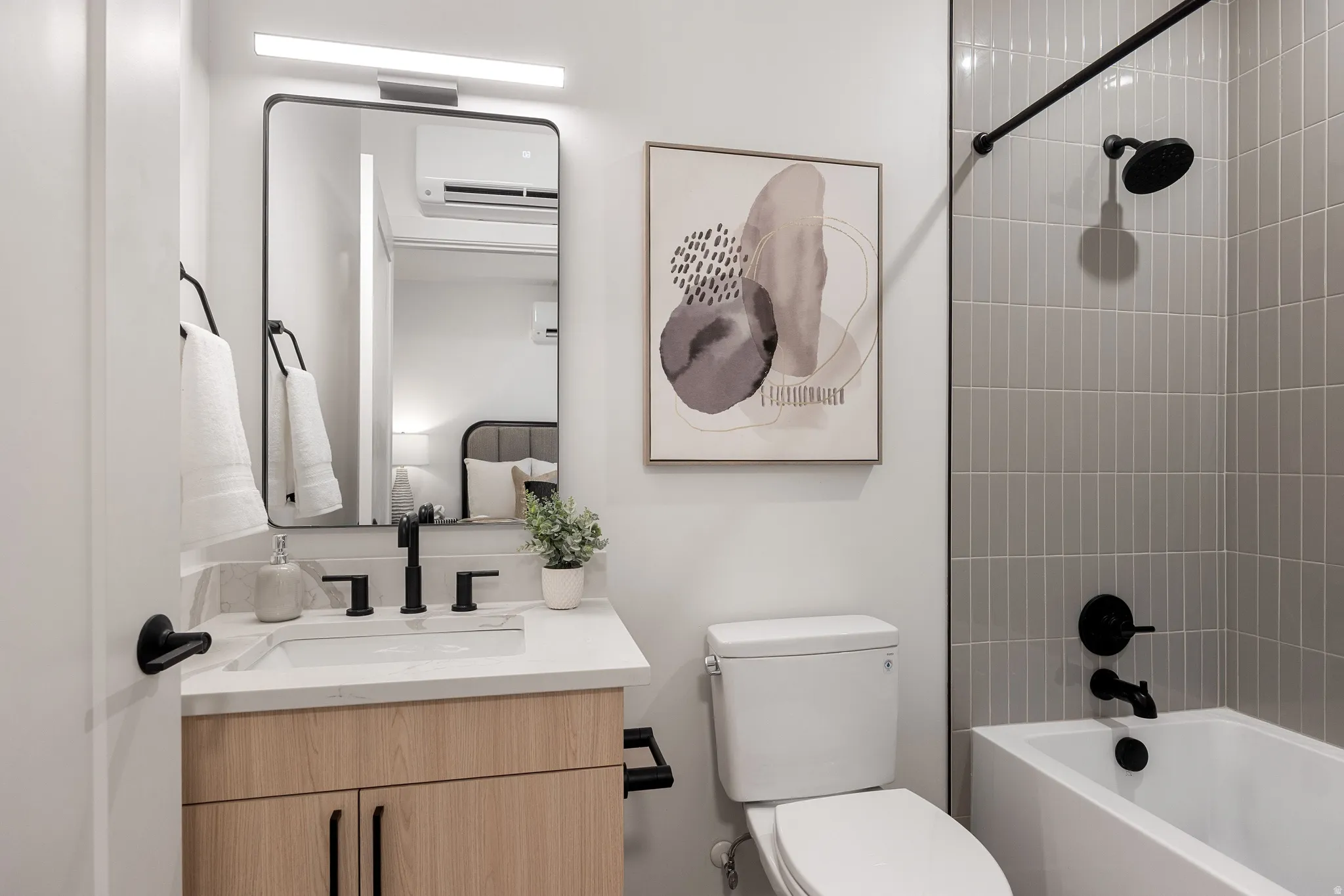 Bathroom featuring a wood-finish vanity with a light-toned countertop, a rectangular mirror, a white toilet, and a bathtub with gray vertical tile surround and matte black fixtures