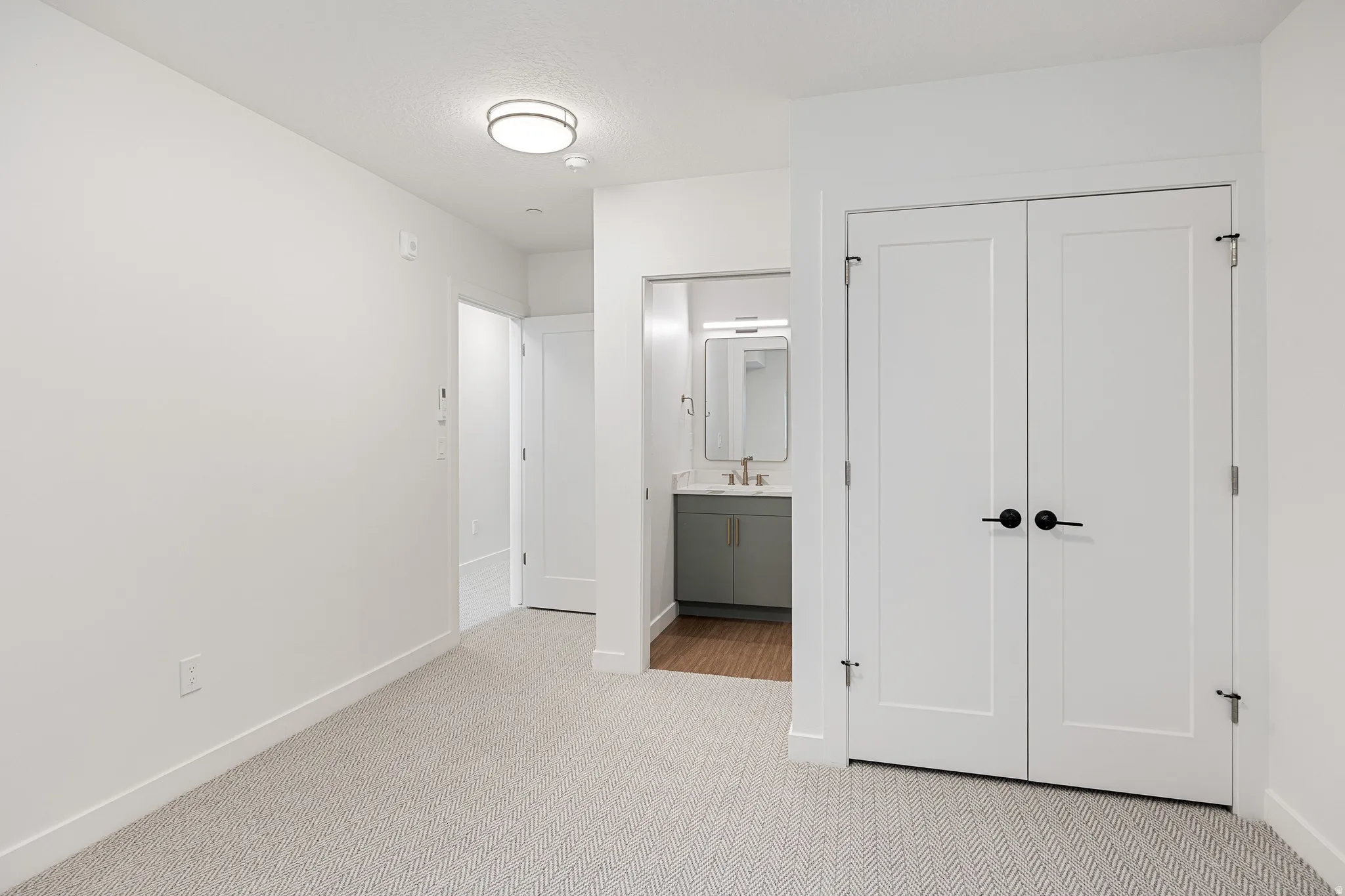 Recessed lighting, wood-finish flooring, white flat-panel doors, matte black hardware, and a vanity with an integrated sink