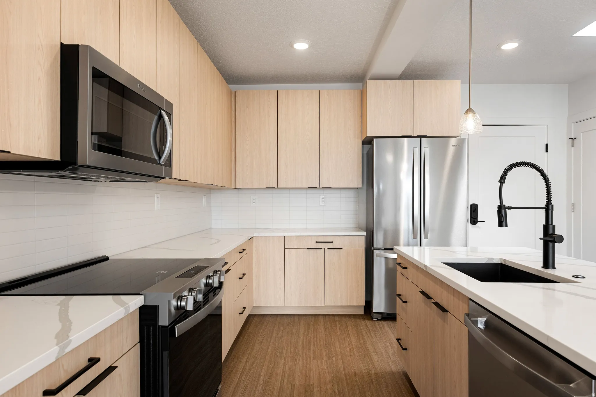 Kitchen featuring light wood-finish cabinetry, white countertops, stainless steel appliances, and a tile backsplash