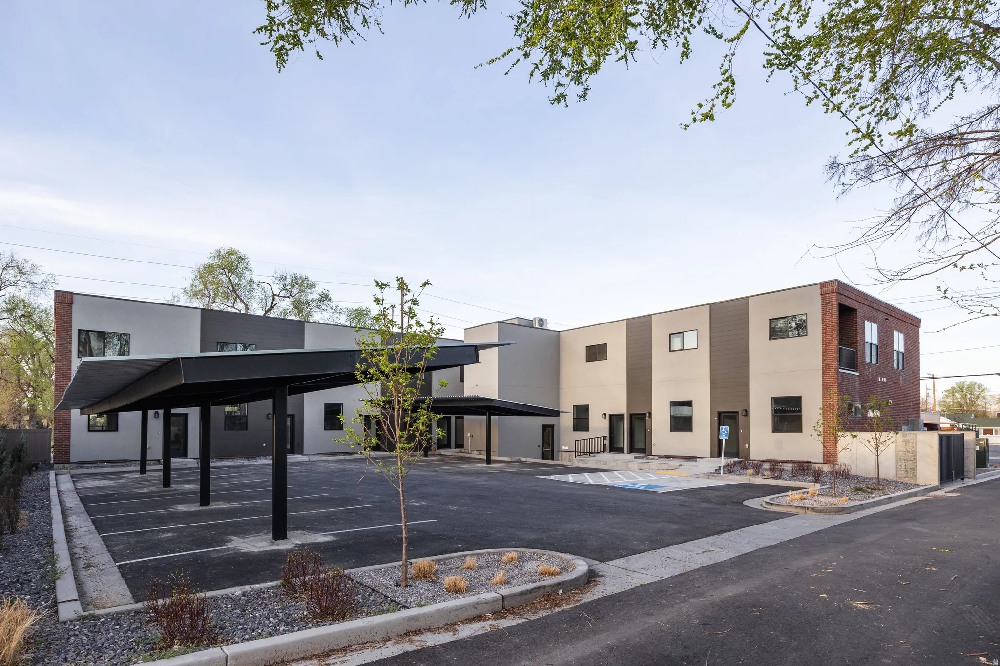 Multi-unit property featuring contemporary architecture with brick accents, covered parking, a paved parking lot, and a designated accessible parking space