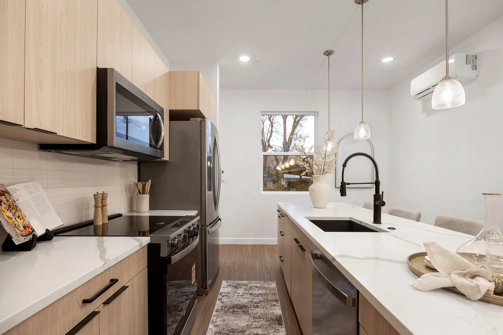 Modern kitchen featuring wood-finish cabinetry, stainless steel appliances, a white subway tile backsplash, and a large island with a black sink and faucet
