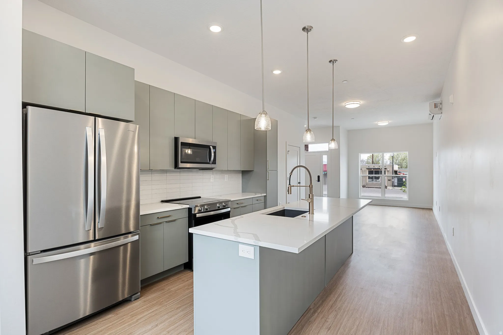 Modern kitchen featuring stainless steel appliances, light-toned cabinetry, a spacious island with an integrated sink, pendant lighting, and wood-finish flooring