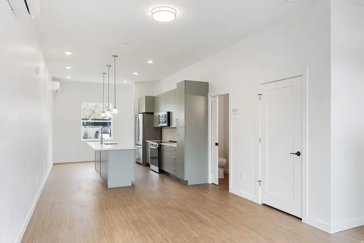 Open-concept living area featuring wood-finish flooring, recessed lighting, and a modern kitchen with a center island and stainless steel appliances