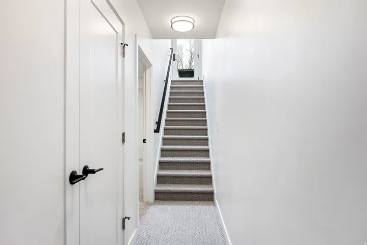 Staircase with carpeted treads and risers, a black handrail, and a round overhead light fixture