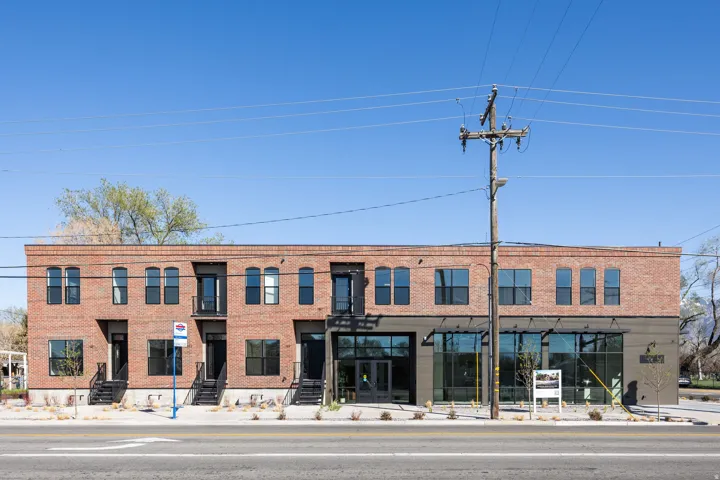 Brick facade with dark-framed windows, ground-level retail spaces, second-story balconies, and multiple entryways