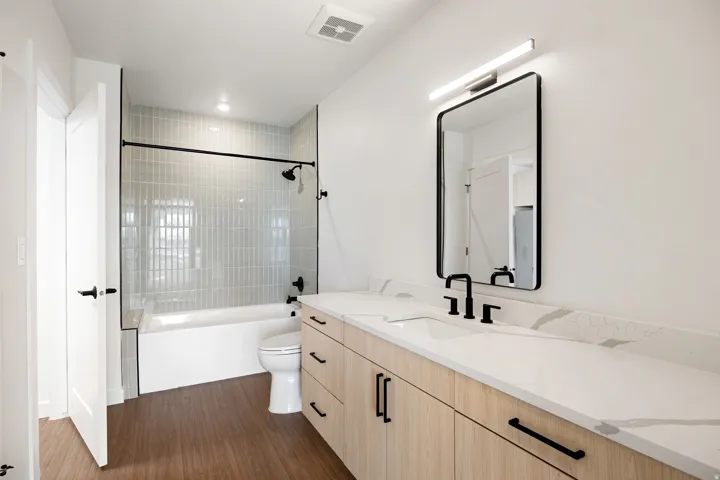 Bathroom featuring a wood-finish double vanity, white countertop, matte black fixtures, framed mirror, and a tiled shower-tub combination