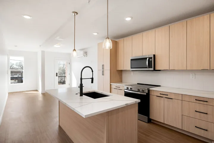 Modern kitchen featuring a large island with an undermount sink, pendant lighting, stainless steel appliances, and wood-finish cabinetry